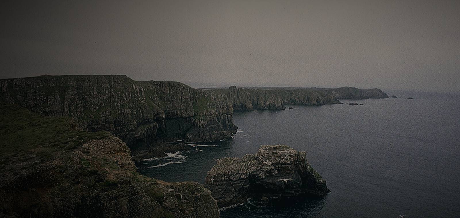 Sea cliffs and rock stacks on Tory Island, County Donegal, seen from the headland of Dún Bhaloir under a grey sky.
