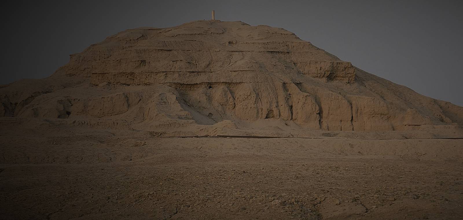 The eroded mud-brick mound of the ziggurat at Uruk rising from flat desert ground.