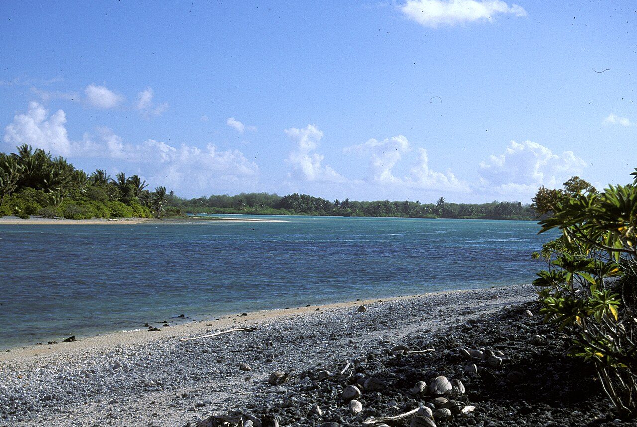 Color photograph of Tatiman Passage, the channel into the lagoon of Nikumaroro (Gardner Island), with green bush on each bank.